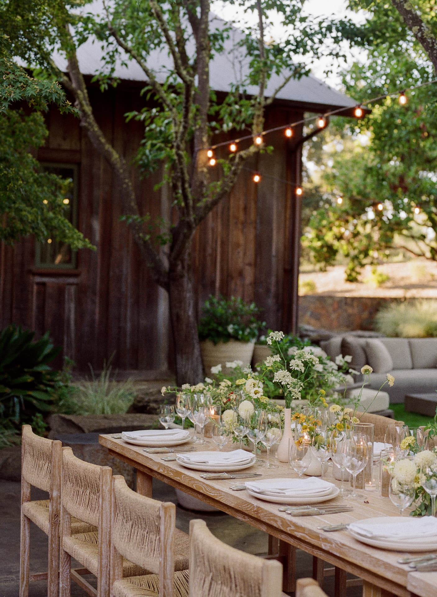 Long dinner table set beneath string lights at a rustic estate